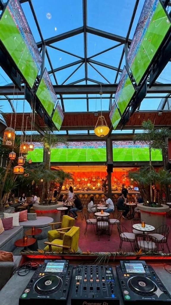 Espacio Kinshasa: lounge con múltiples pantallas de fútbol, ambiente cálido y cabina de DJ